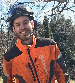 Person i verneklær sager ned tre i hage